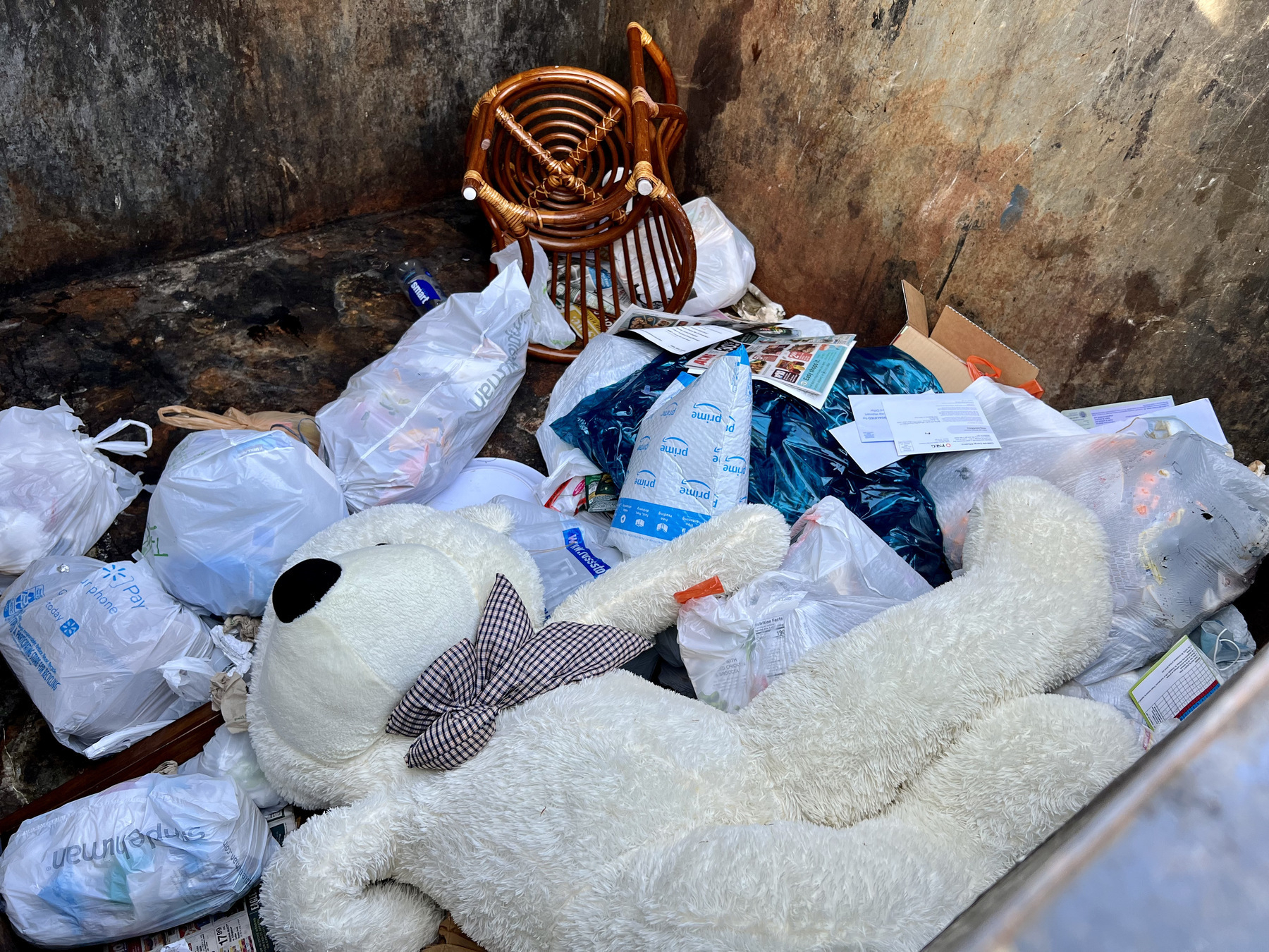 Large teddy bear and chair in dumpster among other trash