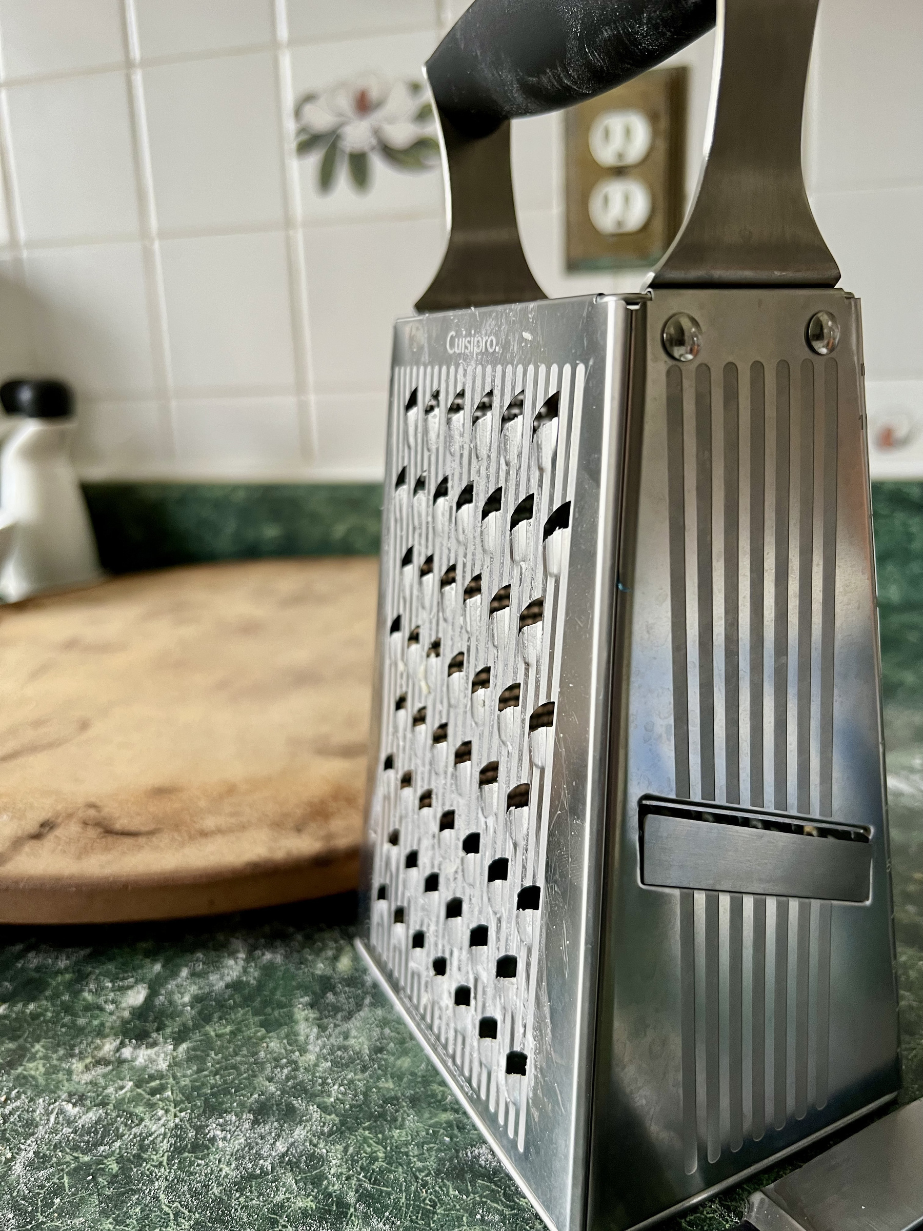 Cheese grater on countertop with pizza stone in background